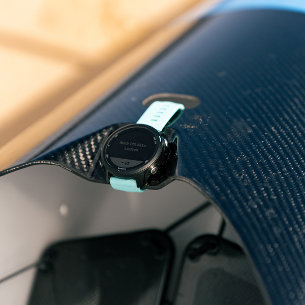 A teal Garmin sport watch mounted to the carbon fiber cockpit of a Synergy high performance canoe for tracking paddling metrics.