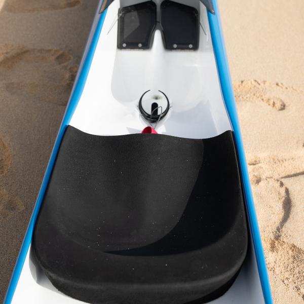 A technical close-up of a Synergy tandem racing canoe from the Nalu collection, highlighting the ergonomic black racing seat and white interior cockpit layout.