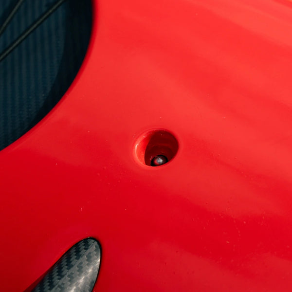 Macro view of a precision-engineered drainage fitting and carbon fiber reinforced section on a red Shaka high-performance outrigger canoe.