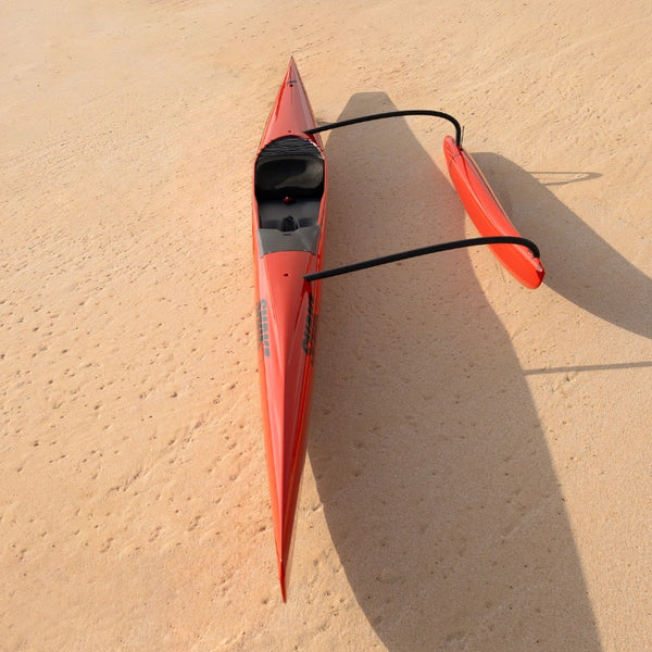 A direct overhead shot of the red Shaka high-performance racing outrigger showcasing its narrow aerodynamic hull and long shadow on the sand.