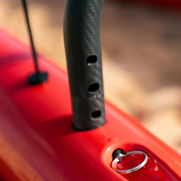 Close-up of an adjustable black carbon fiber iako being secured into the red hull of a Shaka high-performance outrigger canoe.