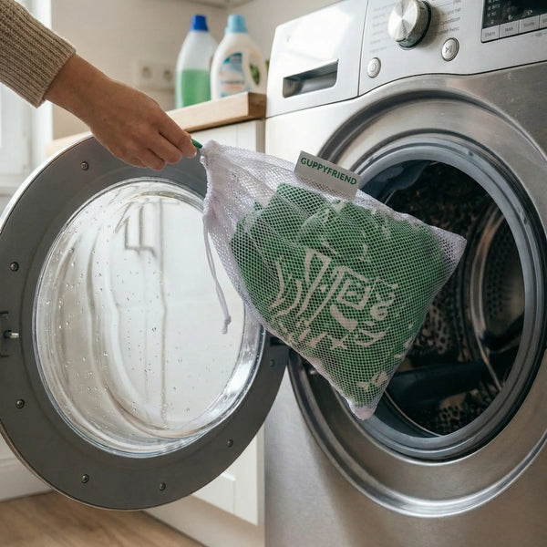 A person places a green tribal-patterned rash guard from the Skild Tattoo collection into a white Guppyfriend washing bag before putting it into a front-loading washing machine.