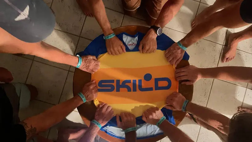 Multiple athletes gather around a table, placing their hands on a vibrant Skild performance jersey from the yellow collection to showcase team unity and branding.
