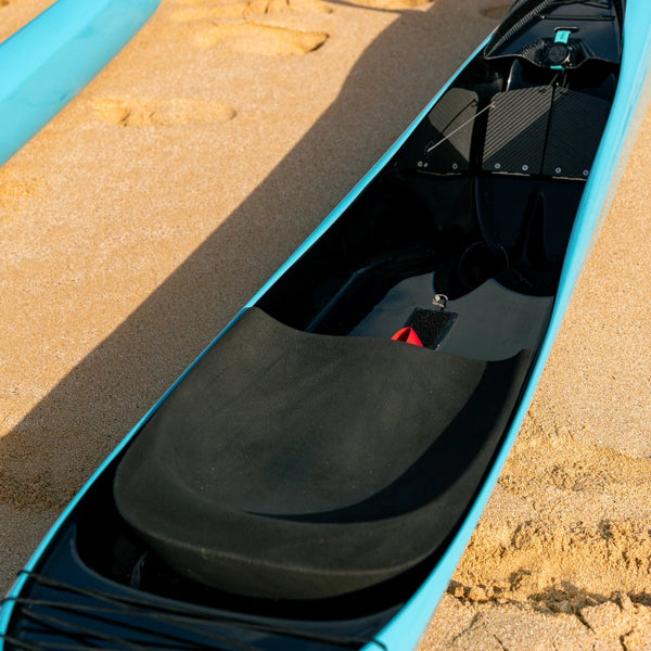 A perspective shot of the Supernova Canoe from the Nalu Outrigger Collection, highlighting the contoured black racing seat and the sleek vibrant blue hull resting on golden sand