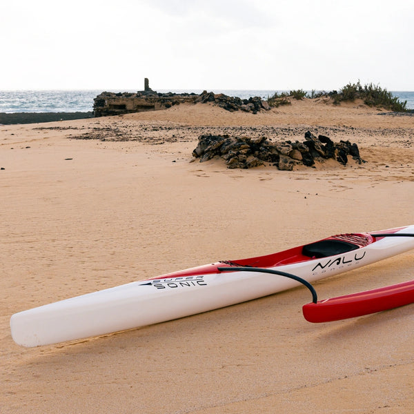 Close-up of the bow of a Nalu outrigger canoe featuring "Super Sonic" branding on a sandy beach with stone ruins in the distance.