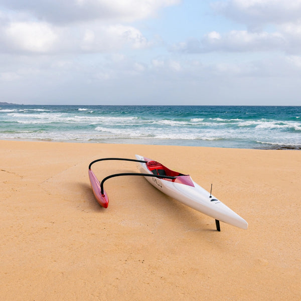 A high-angle view of the open red cockpit and black seat of a white Nalu Supersonic outrigger canoe on the beach.